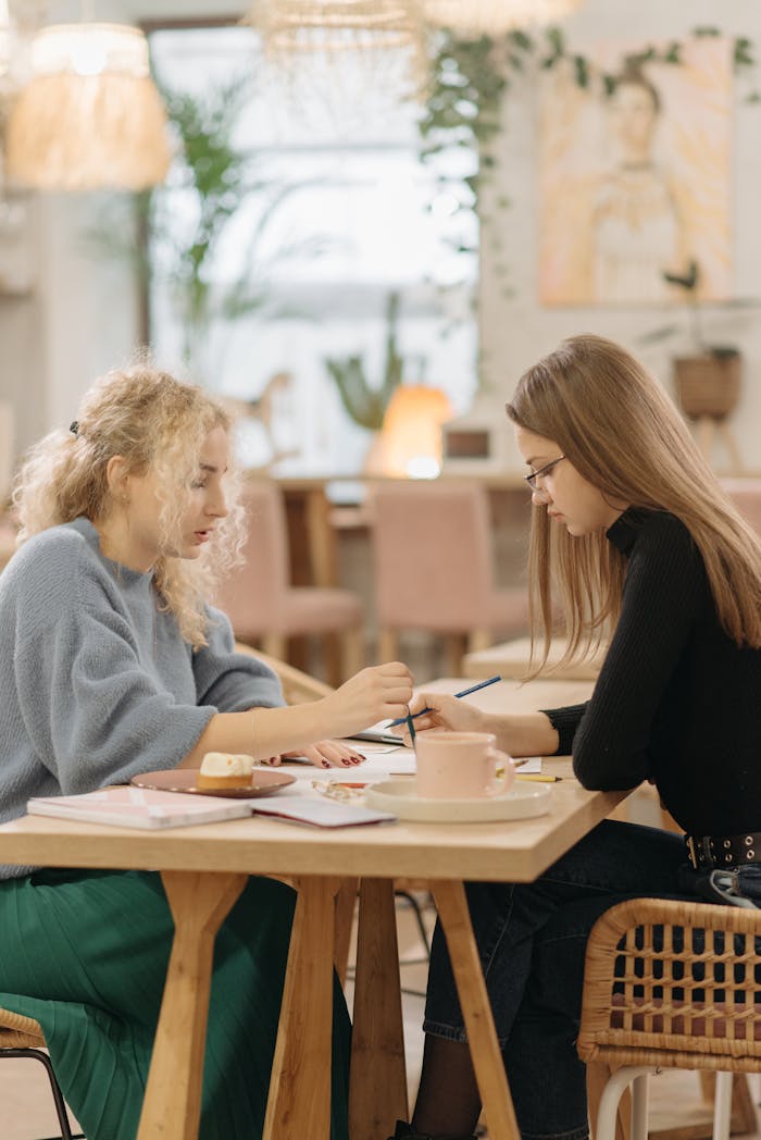 Home Two young women engaged in serious discussion and planning at a cafe table indoors.